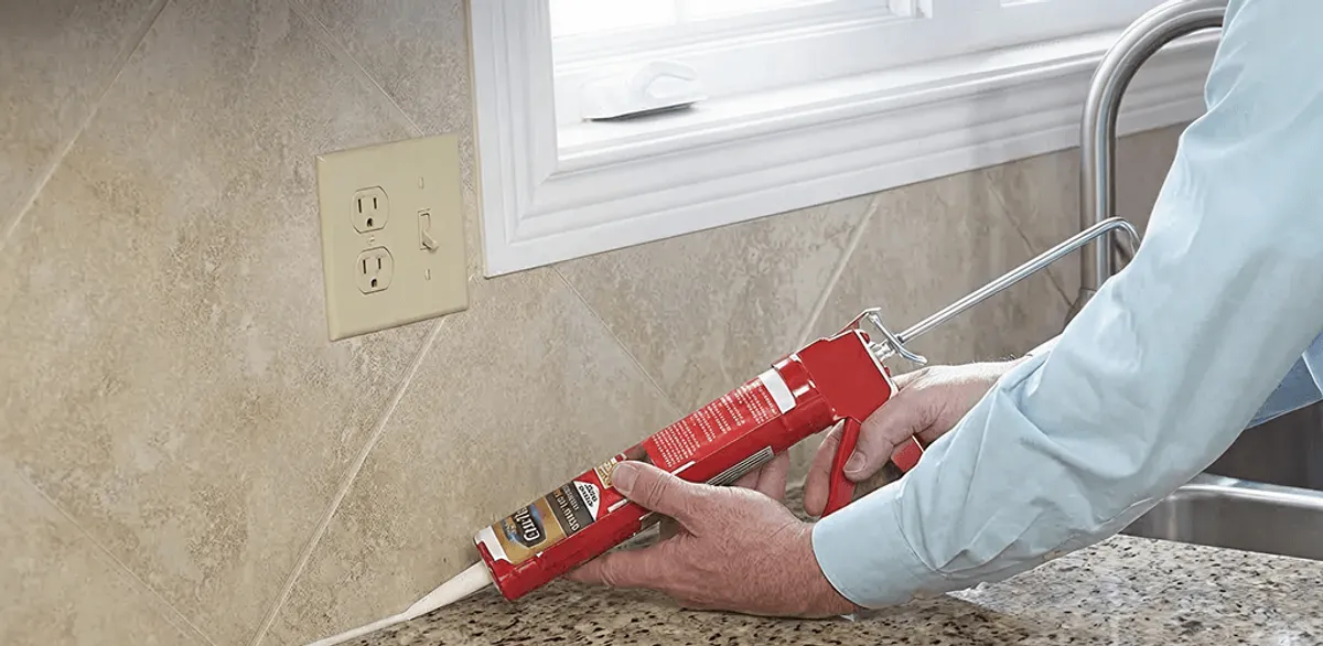 Handyman applying caulk along a kitchen backsplash and countertop seam in Omaha, NE