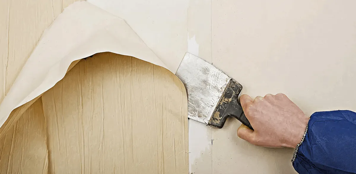 Handyman removing wallpaper with a scraper for wall preparation in Omaha, NE