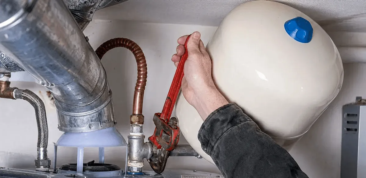Water heater repair technician tightening plumbing connections near a tank unit in Omaha, NE